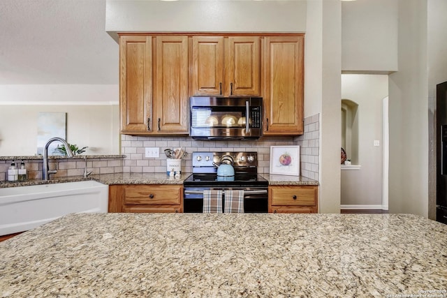 kitchen featuring light stone counters, stainless steel microwave, a sink, and black electric range oven