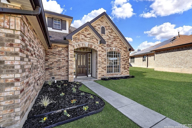 entrance to property featuring a shingled roof, brick siding, and a lawn