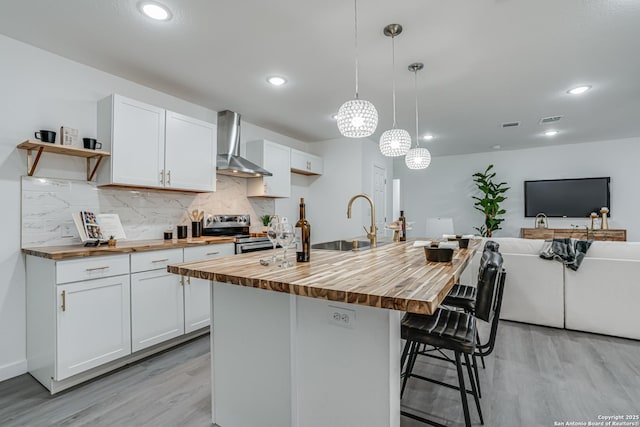 kitchen with butcher block countertops, a sink, electric stove, wall chimney range hood, and decorative backsplash