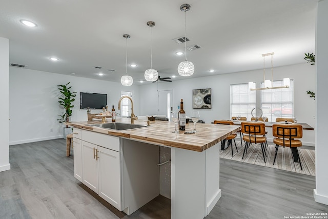 kitchen with wooden counters, a sink, visible vents, and white cabinetry