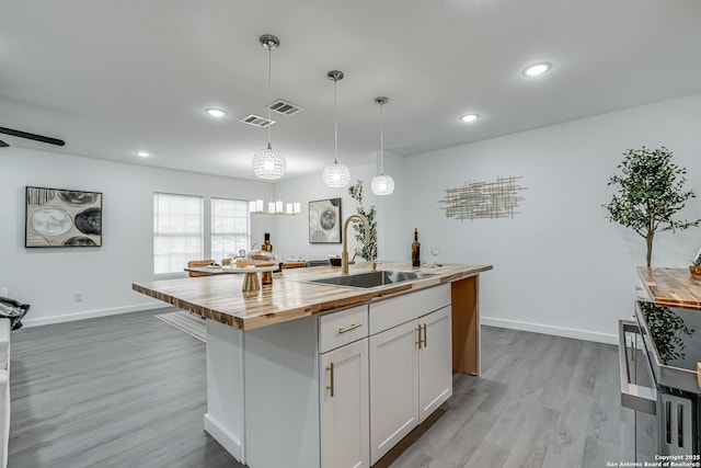 kitchen with butcher block counters, a sink, visible vents, light wood-type flooring, and an island with sink