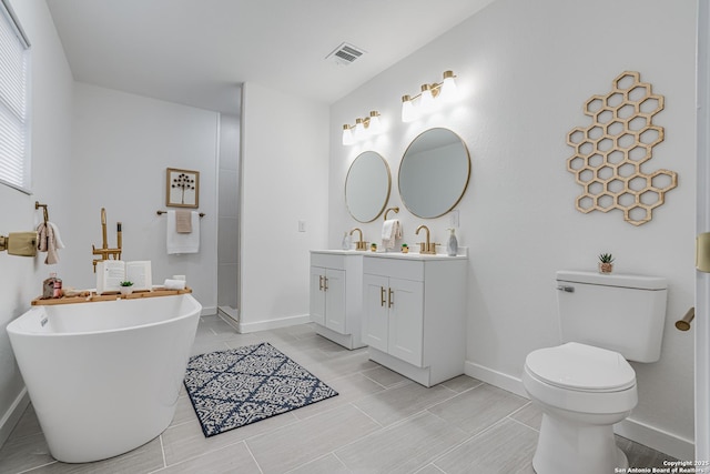 full bathroom with toilet, vanity, visible vents, a freestanding bath, and baseboards