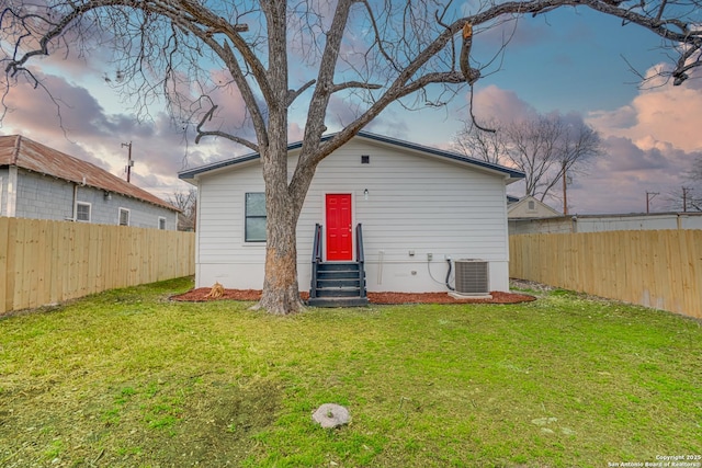 back of property at dusk featuring entry steps, a yard, a fenced backyard, and cooling unit