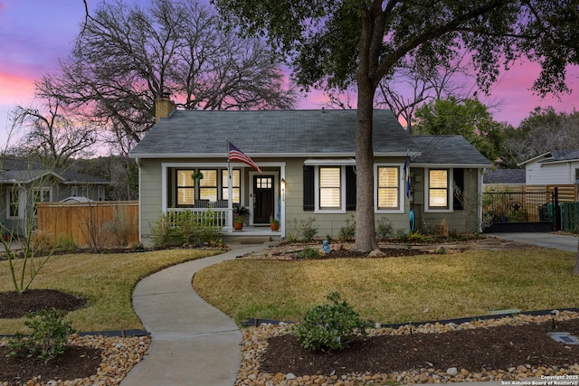 bungalow with a shingled roof, a chimney, fence, a yard, and a porch