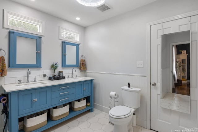 full bath with a wainscoted wall, toilet, a sink, and visible vents