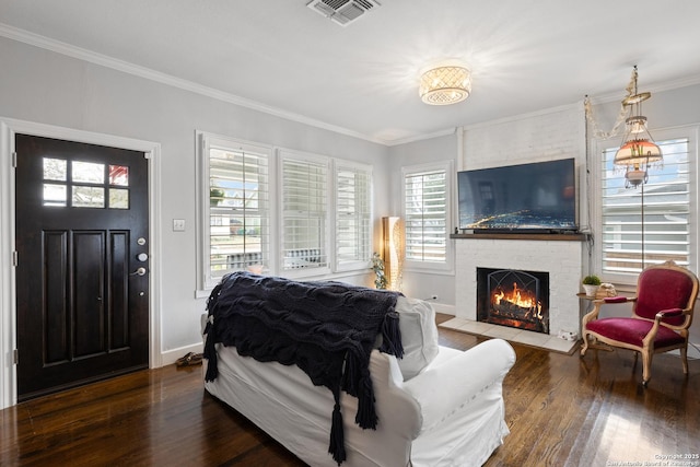 living area featuring visible vents, baseboards, a brick fireplace, hardwood / wood-style floors, and crown molding