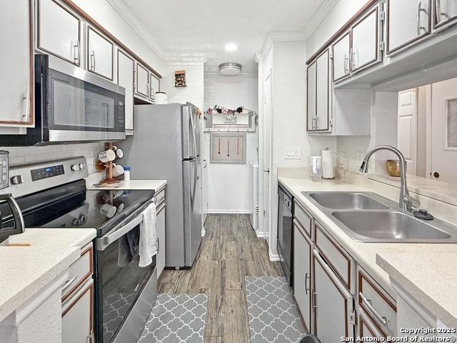 kitchen with stainless steel appliances, backsplash, dark wood-type flooring, ornamental molding, and a sink