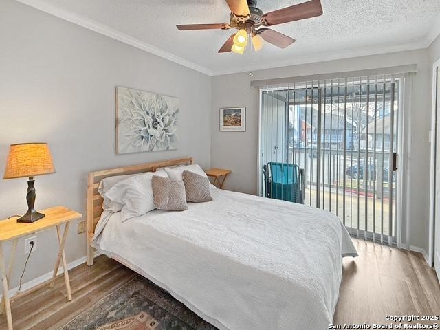 bedroom with a textured ceiling, ornamental molding, wood finished floors, and access to exterior