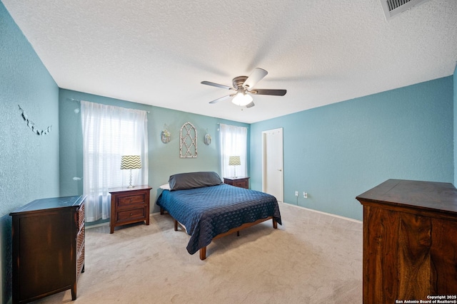 bedroom with a textured wall, multiple windows, visible vents, and light colored carpet