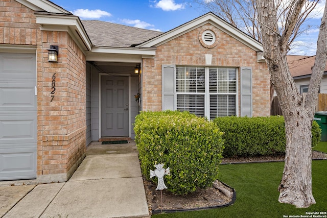 property entrance featuring a garage, a yard, brick siding, and roof with shingles