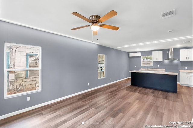 kitchen with wood finished floors, visible vents, white cabinetry, a center island, and wall chimney exhaust hood