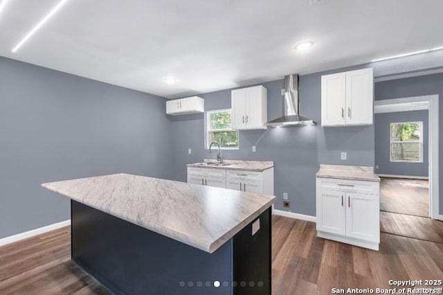 kitchen with wall chimney range hood, dark wood-type flooring, a sink, and white cabinetry