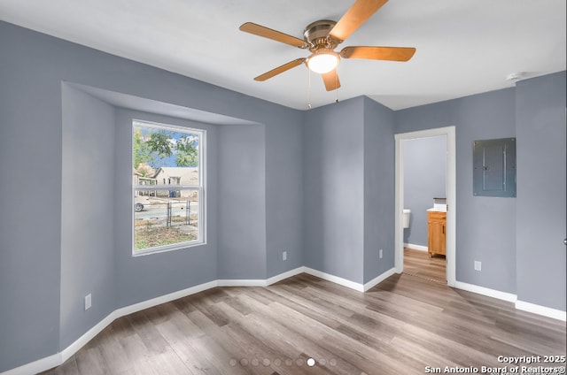 empty room featuring a ceiling fan, electric panel, baseboards, and wood finished floors