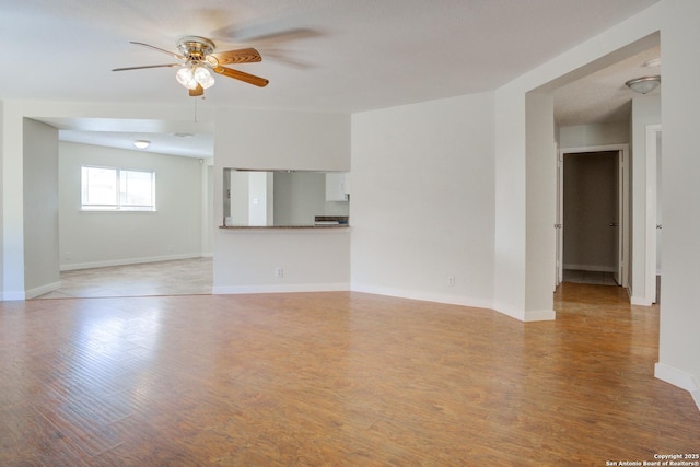 empty room with ceiling fan, light wood finished floors, and baseboards