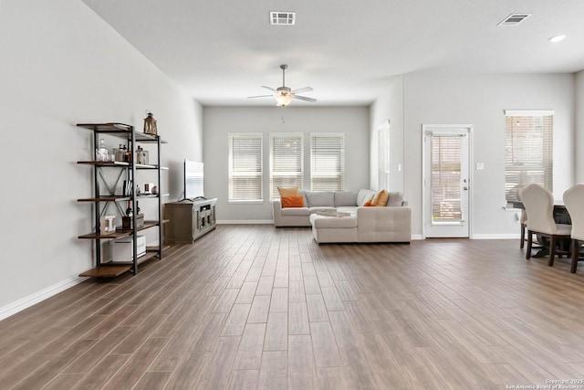 living area with a ceiling fan, visible vents, baseboards, and wood finished floors