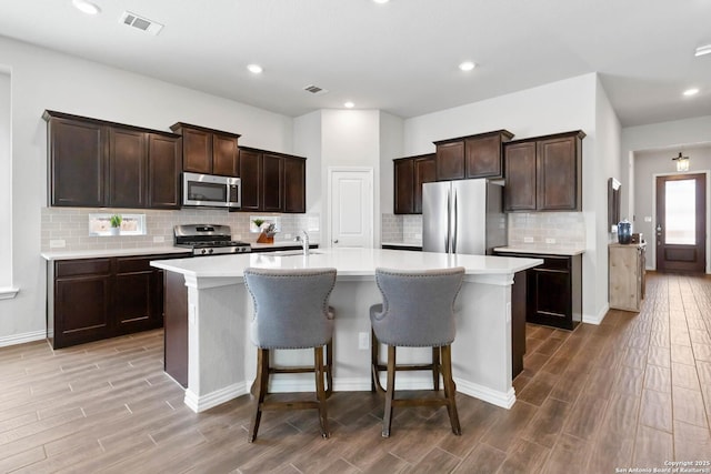 kitchen with visible vents, light countertops, appliances with stainless steel finishes, wood tiled floor, and an island with sink