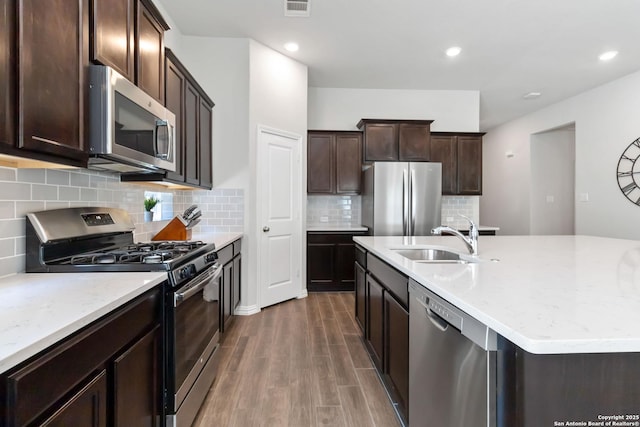 kitchen with dark brown cabinetry, dark wood-style flooring, a sink, appliances with stainless steel finishes, and a center island with sink