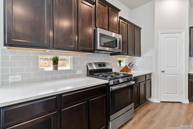 kitchen with dark brown cabinets, appliances with stainless steel finishes, backsplash, and light wood-style flooring