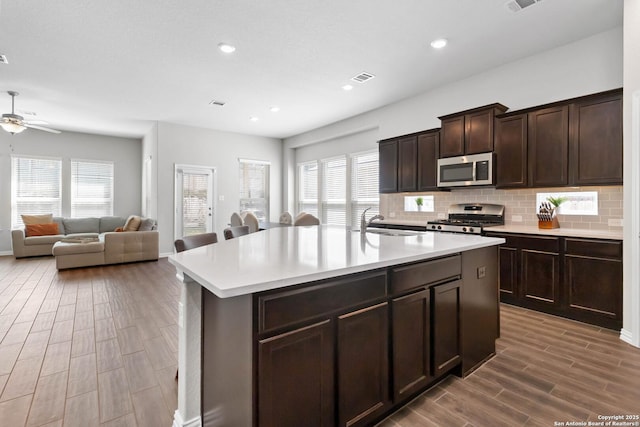 kitchen with stainless steel appliances, wood finish floors, visible vents, light countertops, and decorative backsplash