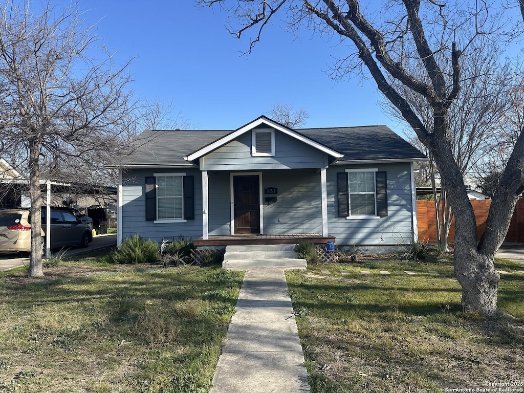 bungalow-style home featuring covered porch, fence, a front lawn, and a carport