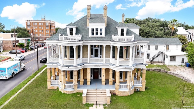 back of property with a porch, a balcony, roof with shingles, a lawn, and a chimney