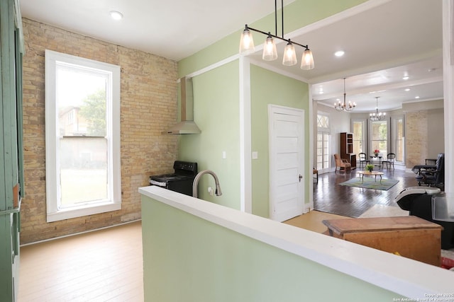 kitchen featuring a sink, wall chimney range hood, black electric range oven, light wood finished floors, and an inviting chandelier