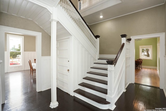 staircase with ornamental molding, wainscoting, and wood finished floors