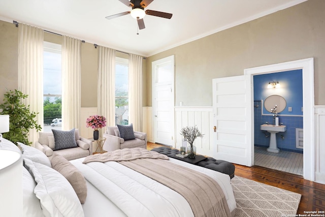 bedroom featuring ceiling fan, ensuite bathroom, and wainscoting