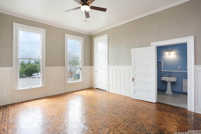 unfurnished room featuring a healthy amount of sunlight, a wainscoted wall, and a ceiling fan