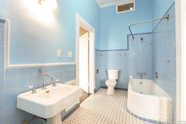 bathroom featuring toilet, a sink, tile walls, tub / shower combination, and wainscoting