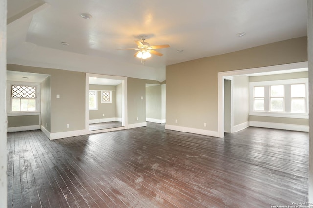 unfurnished living room featuring dark wood-type flooring, a healthy amount of sunlight, baseboards, and a ceiling fan