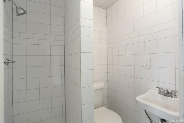 bathroom featuring a tile shower, a sink, and toilet