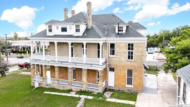 rear view of house with brick siding, a porch, a shingled roof, a lawn, and a balcony