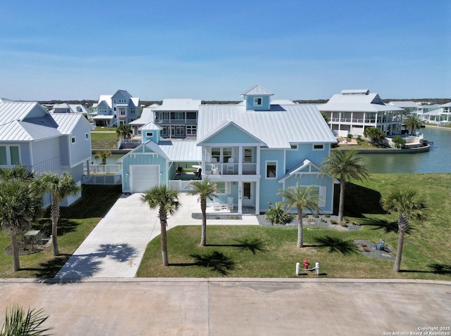 view of front facade featuring concrete driveway, a front yard, a standing seam roof, a balcony, and a garage