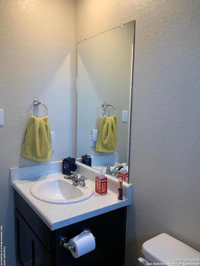 bathroom featuring toilet, a textured wall, and vanity