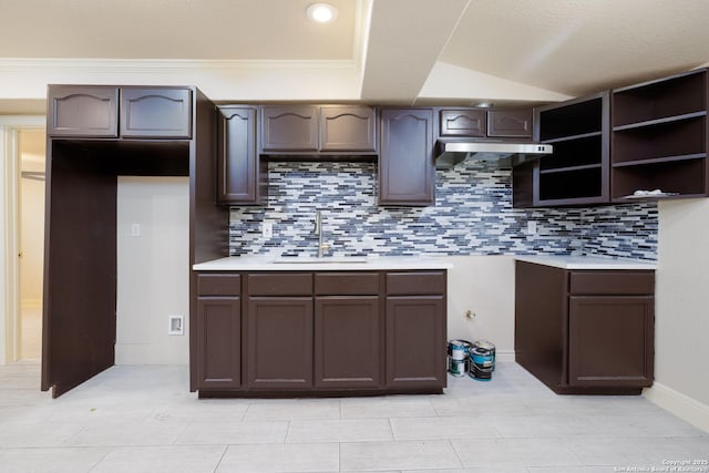 kitchen featuring light countertops, a sink, dark brown cabinetry, and under cabinet range hood