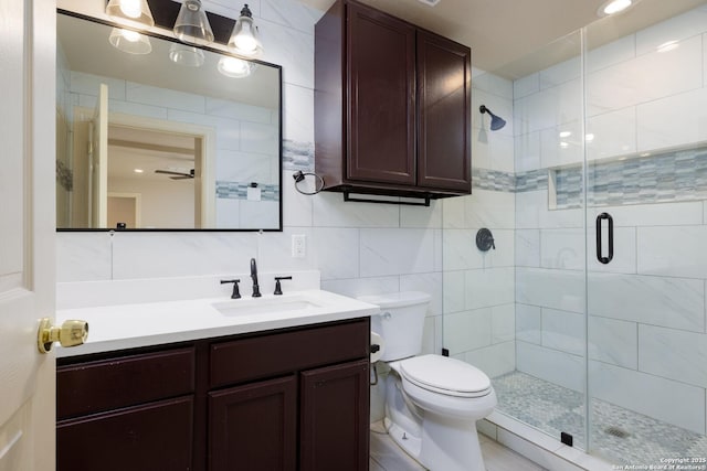 bathroom with toilet, a shower stall, tile walls, and vanity