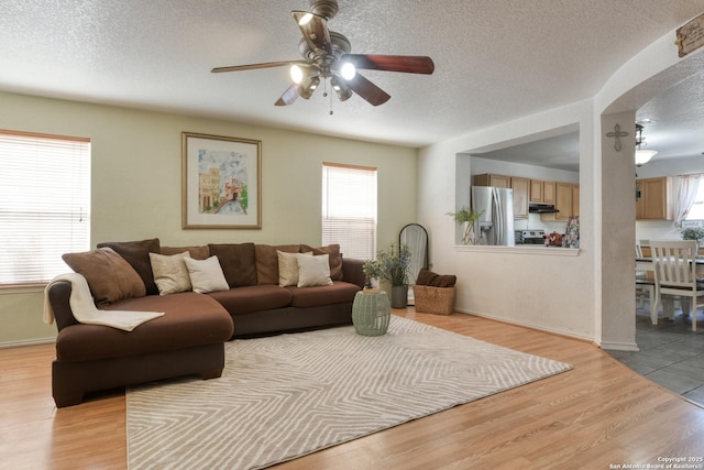 living area with a ceiling fan, light wood-style floors, baseboards, and a textured ceiling