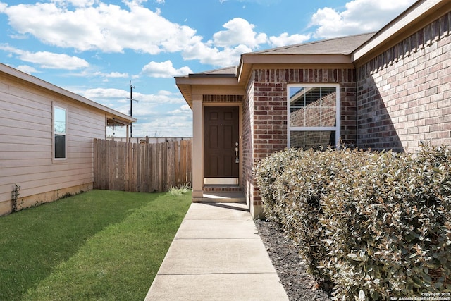 entrance to property with brick siding, a lawn, and fence