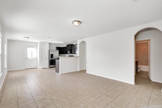 unfurnished living room with arched walkways, baseboards, and light tile patterned floors