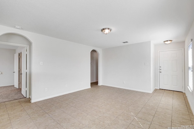 spare room with arched walkways, light tile patterned flooring, visible vents, and baseboards