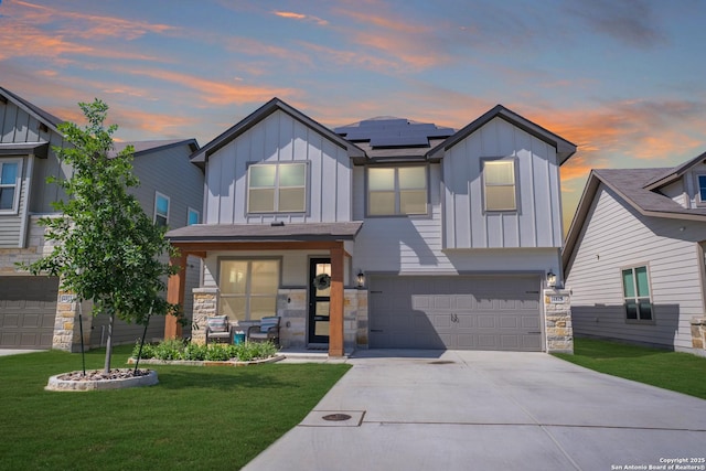 view of front of property with a garage, roof mounted solar panels, board and batten siding, and a front yard