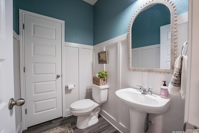 bathroom with wainscoting, wood finished floors, toilet, and a decorative wall