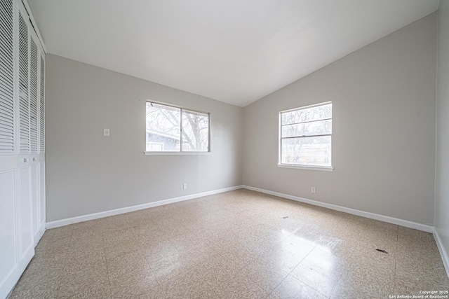 unfurnished room featuring a healthy amount of sunlight, baseboards, and vaulted ceiling