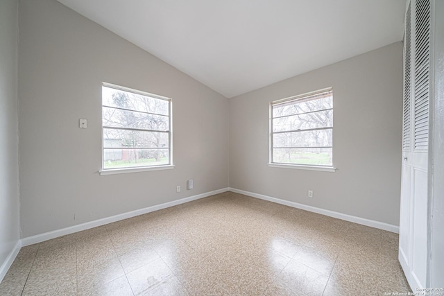 spare room with vaulted ceiling, tile patterned floors, a wealth of natural light, and baseboards