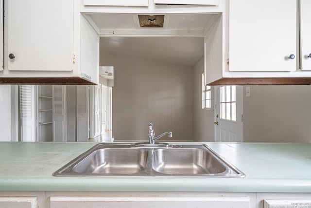 kitchen with light countertops, vaulted ceiling, white cabinets, and a sink