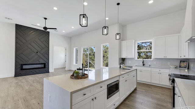 kitchen with stainless steel appliances, recessed lighting, hanging light fixtures, light wood-style floors, and a sink