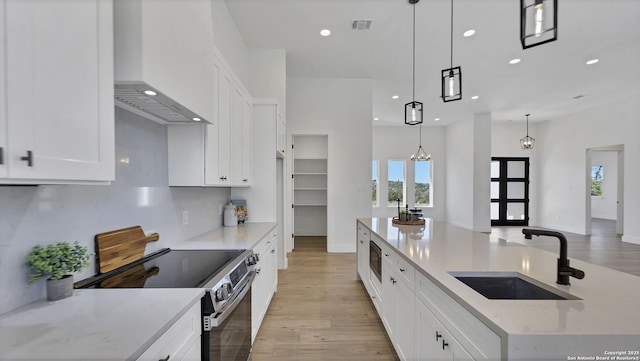 kitchen with stainless steel appliances, visible vents, a sink, wall chimney range hood, and an island with sink