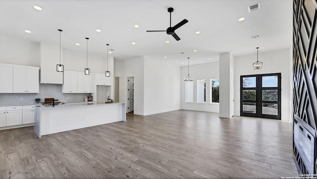 kitchen with tasteful backsplash, visible vents, a towering ceiling, french doors, and light wood-style floors