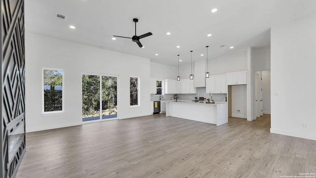 unfurnished living room featuring a towering ceiling, light wood finished floors, ceiling fan, and visible vents